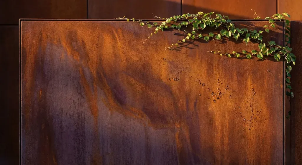 Primer plano de la textura oxidada de un panel de acero corten con tonos naranjas y marrones en un jardín de diseño.