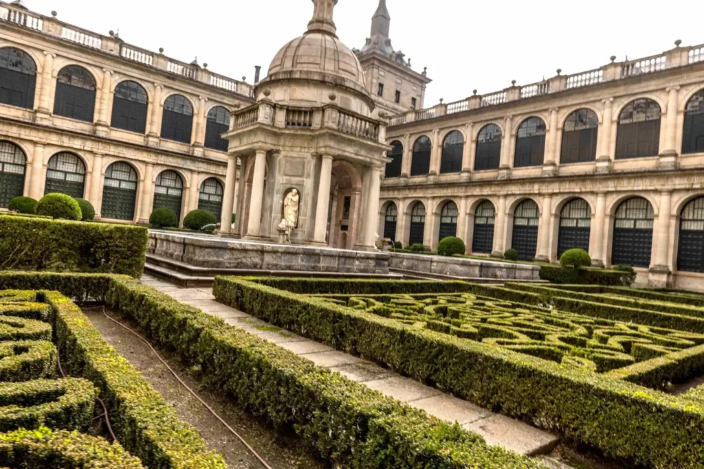 Templete de granito de Juan de Herrera en el Patio de los Evangelistas, rodeado de setos de boj recortados con rigor renacentista.