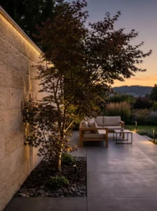 Iluminación indirecta sobre un muro de piedra y un arce japonés creando una atmósfera de calidad visual sin mostrar la tecnología