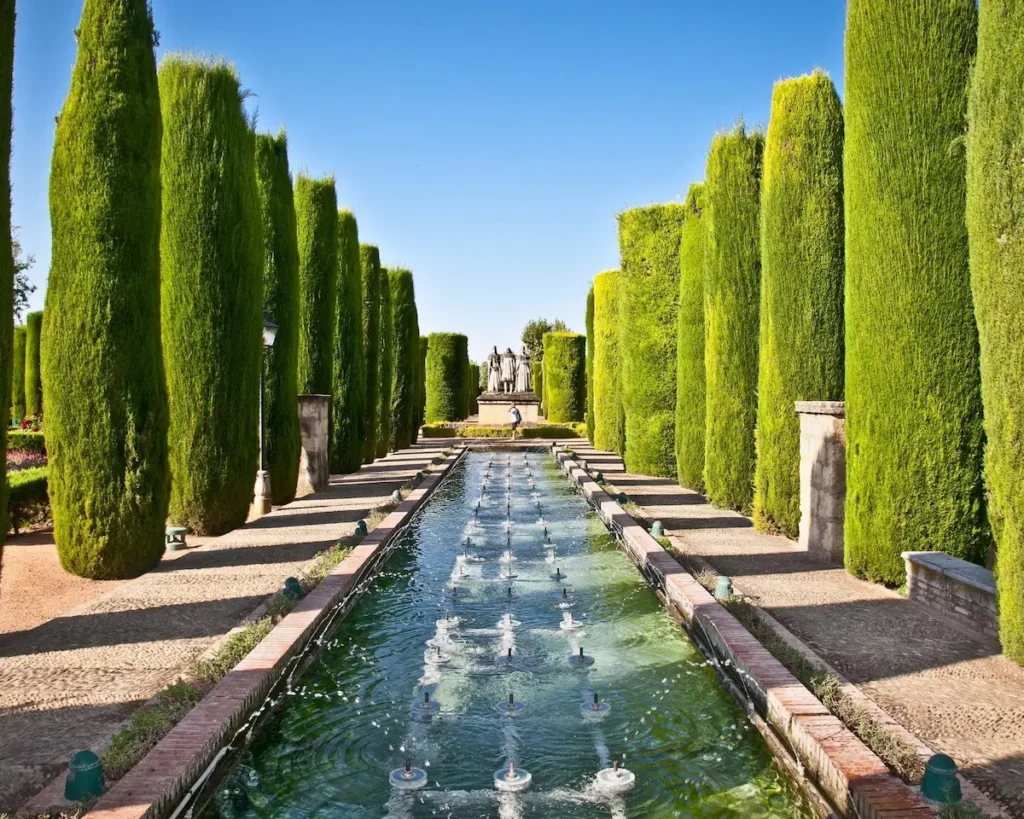 acequia del Paseo de los Reyes flanqueada por cipreses alineados y al fondo grupo escultórico con los Reyes Católicos