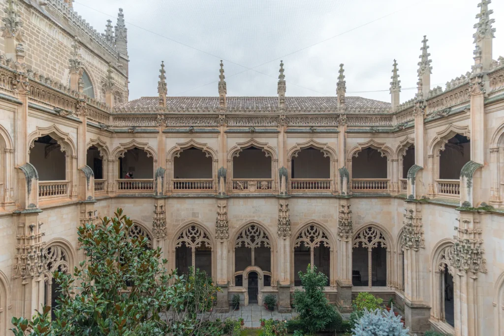 Perspectiva general del claustro del Monasterio de San Juan de los Reyes en Toledo, mostrando la transición orgánica entre la arquitectura gótica y la composición vegetal.